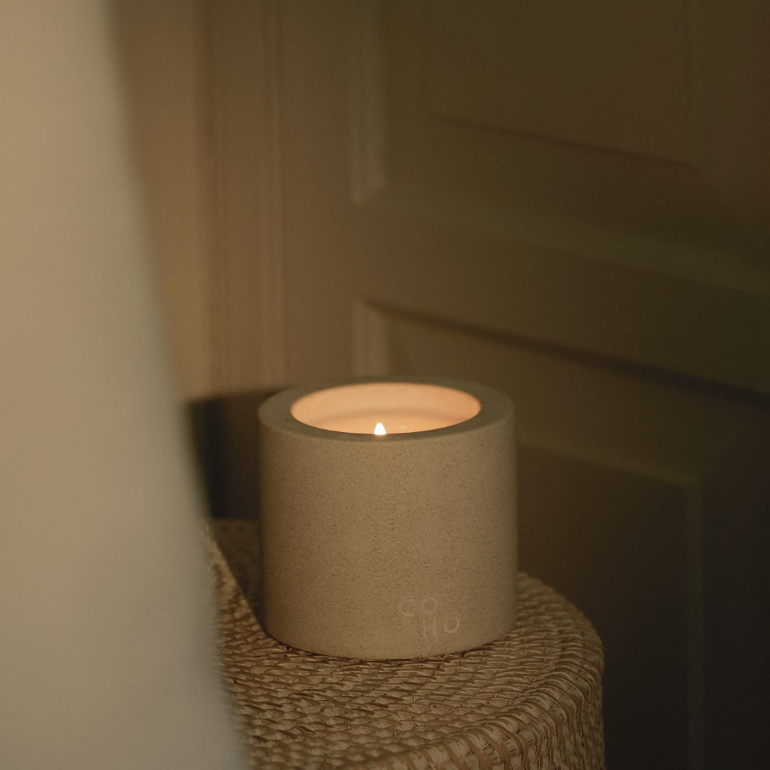 Concrete candle holder with a lit candle on a textured surface.